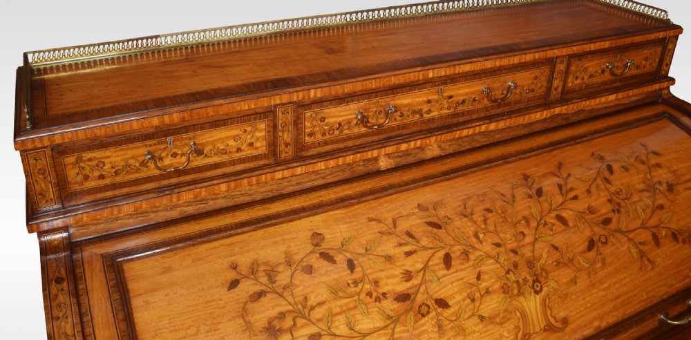 A Sheraton Revival satinwood cylinder bureau featuring detailed floral marquetry inlays, a curved roll-top front, brass gallery, and multiple drawers raised on tapered square legs. View X