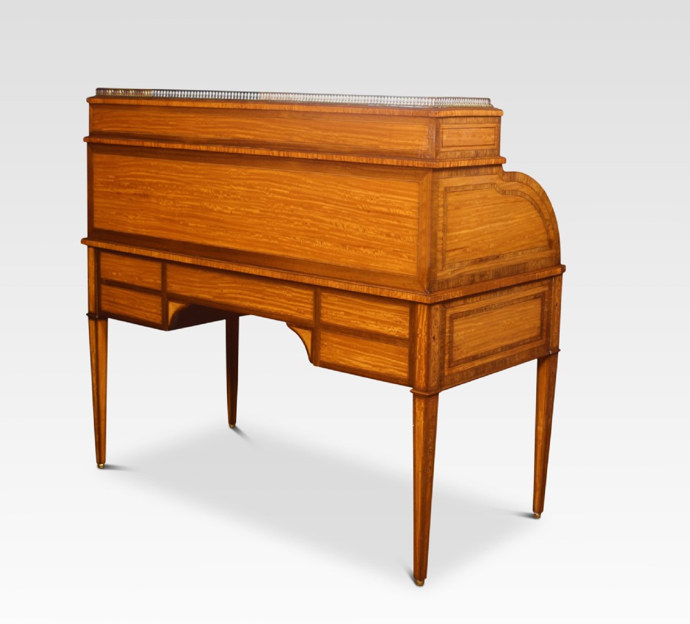 A Sheraton Revival satinwood cylinder bureau featuring detailed floral marquetry inlays, a curved roll-top front, brass gallery, and multiple drawers raised on tapered square legs. View XI