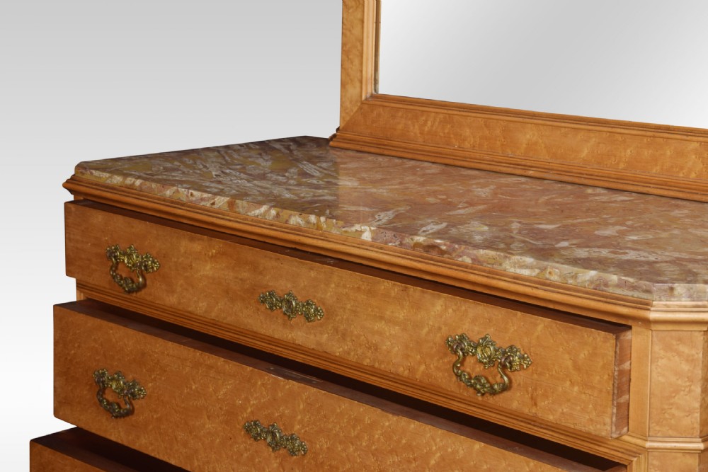 An antique birds eye maple chest of four drawers featuring a marble top, ornate brass handles, and a large arched mirror framed by a carved foliate crest. View VI