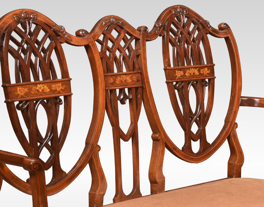 An Edwardian inlaid mahogany settee featuring a triple shield-back design with openwork lattice fretwork, floral marquetry, curved arms, and an upholstered seat. View V