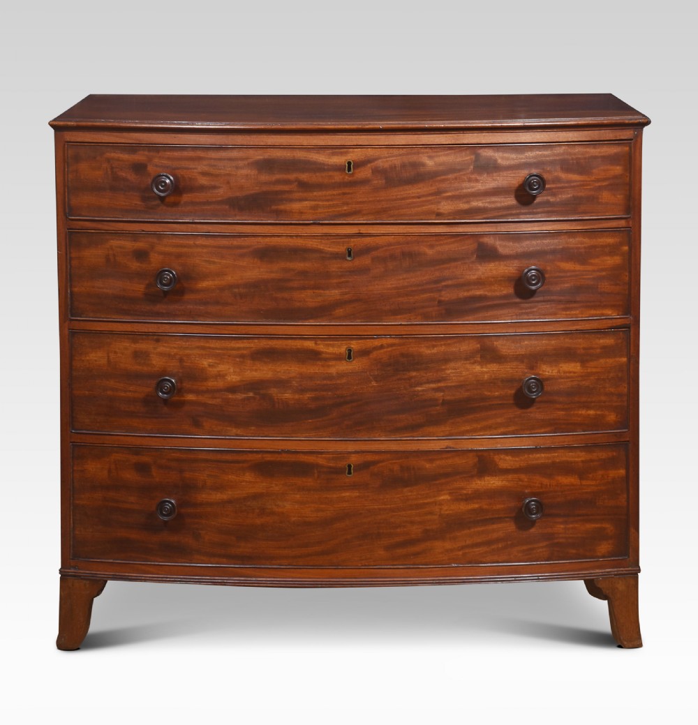 An antique Regency flame mahogany chest featuring four curved bow-front drawers with turned wooden knobs and splayed bracket feet.