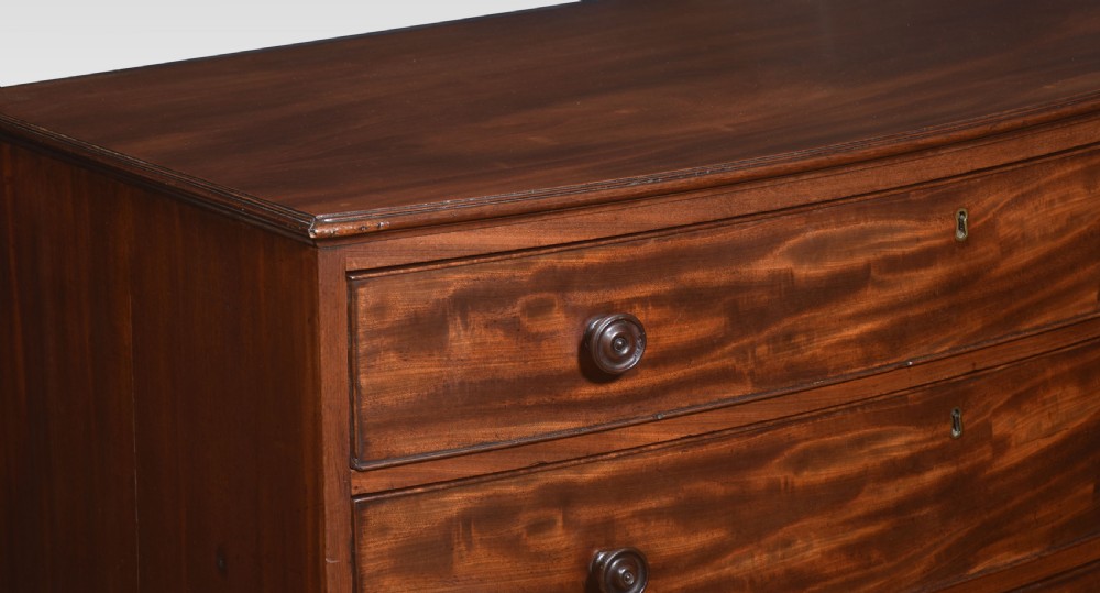 An antique Regency flame mahogany chest featuring four curved bow-front drawers with turned wooden knobs and splayed bracket feet. View III
