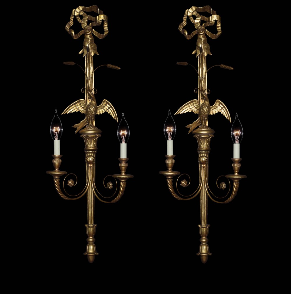 A pair of carved giltwood two-branch wall lights featuring top ribbon bows, carved birds, and fluted central shafts.