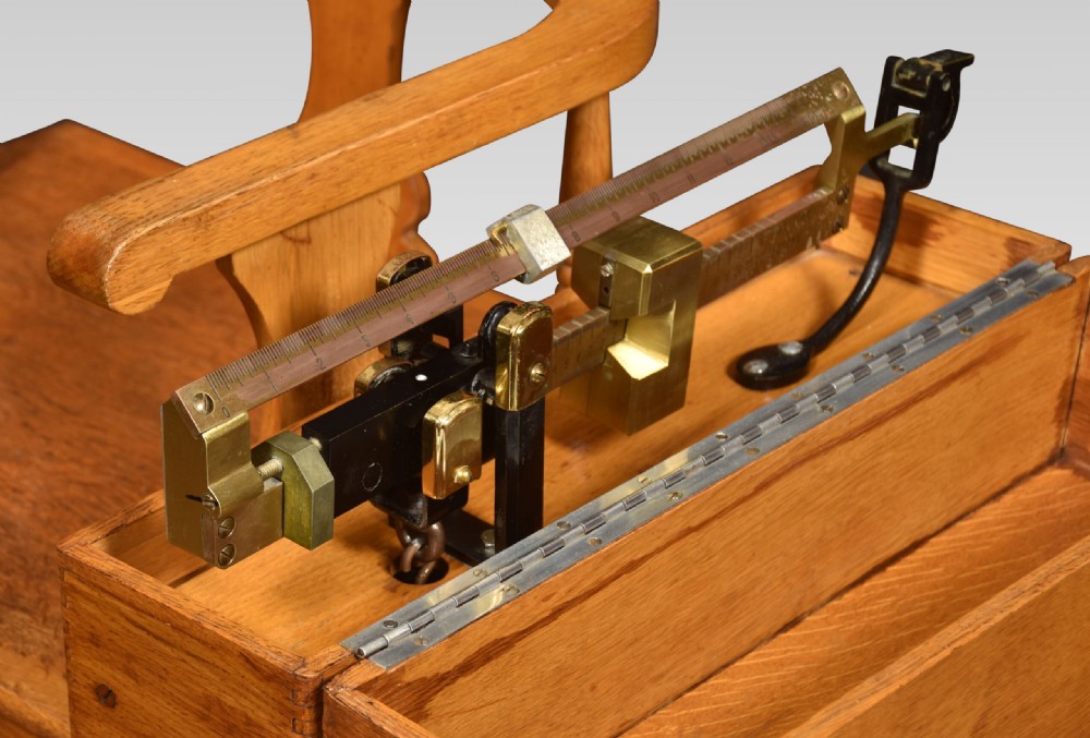 An antique oak doctors weighing scale chair with two spoked wheels, a wooden armchair frame, and a side-mounted brass weighing beam mechanism. View IV