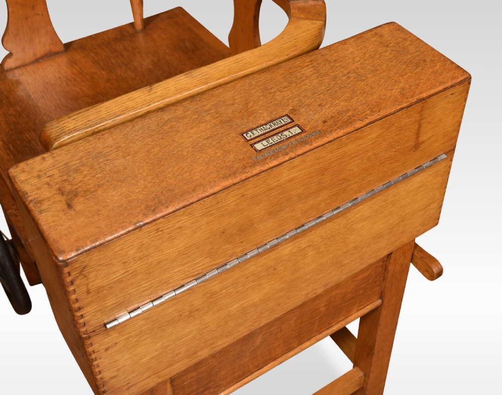 An antique oak doctors weighing scale chair with two spoked wheels, a wooden armchair frame, and a side-mounted brass weighing beam mechanism. View V
