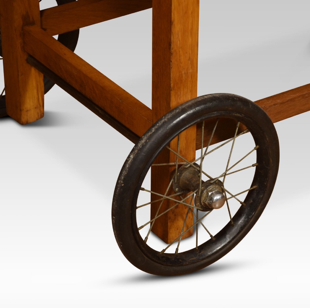An antique oak doctors weighing scale chair with two spoked wheels, a wooden armchair frame, and a side-mounted brass weighing beam mechanism. View VII