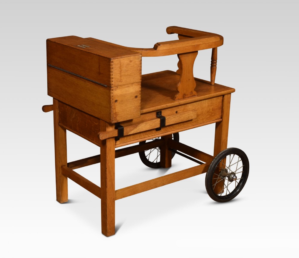 An antique oak doctors weighing scale chair with two spoked wheels, a wooden armchair frame, and a side-mounted brass weighing beam mechanism. View VIII