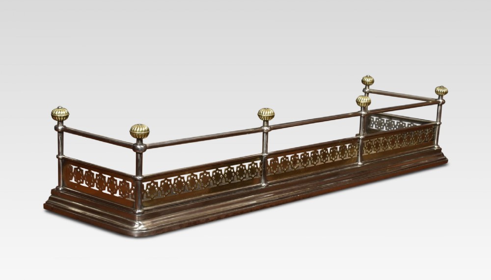 A Georgian polished steel and brass fireplace fender featuring a pierced geometric band, upper rail, and fluted brass finials.