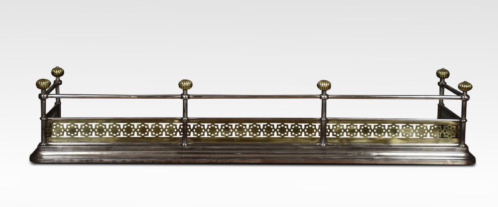A Georgian polished steel and brass fireplace fender featuring a pierced geometric band, upper rail, and fluted brass finials. View II