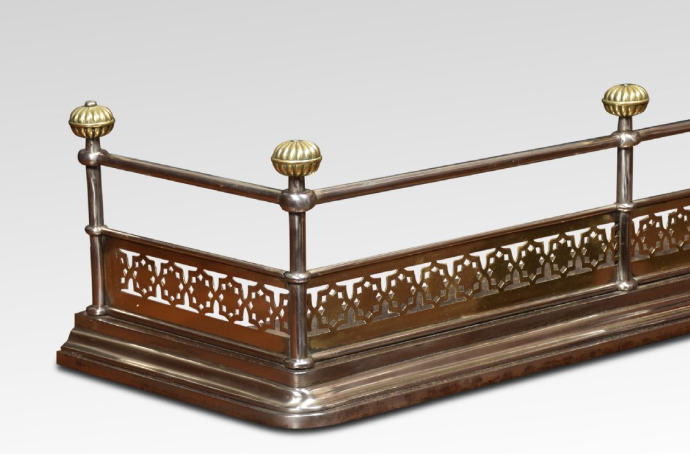 A Georgian polished steel and brass fireplace fender featuring a pierced geometric band, upper rail, and fluted brass finials. View III