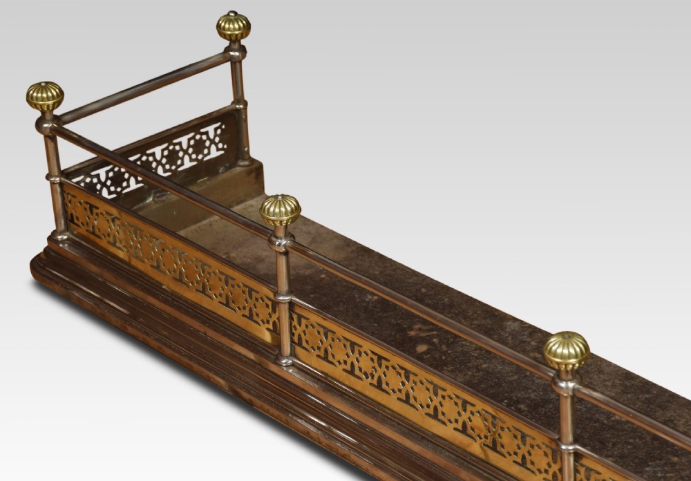 A Georgian polished steel and brass fireplace fender featuring a pierced geometric band, upper rail, and fluted brass finials. View VI