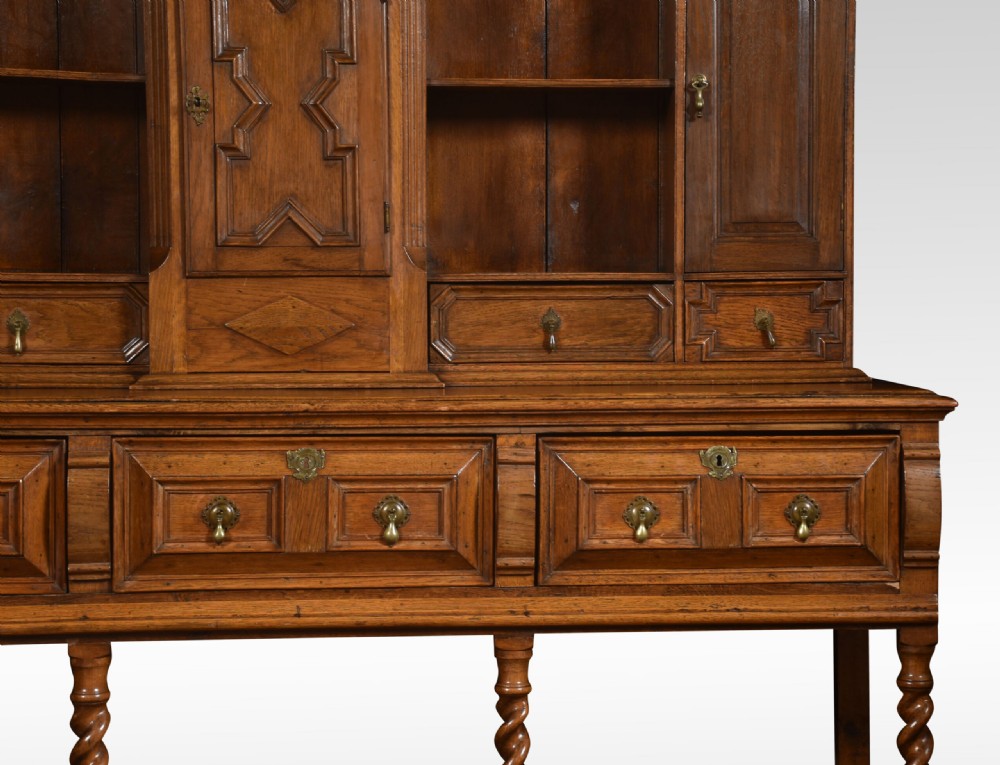 A Jacobean style oak dresser featuring geometric panel moulding, a central integrated clock, open upper shelves, and six barley twist legs. View II