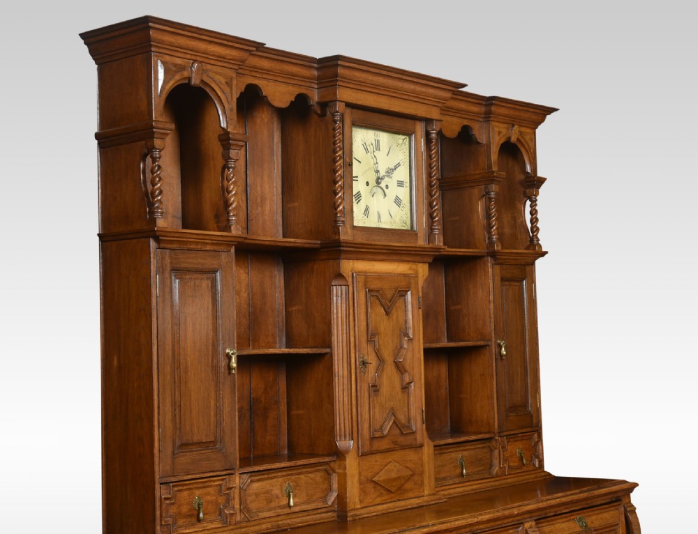 A Jacobean style oak dresser featuring geometric panel moulding, a central integrated clock, open upper shelves, and six barley twist legs. View V