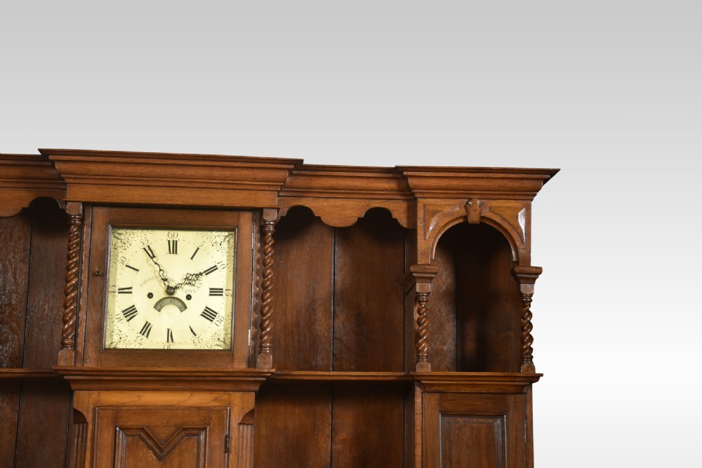 A Jacobean style oak dresser featuring geometric panel moulding, a central integrated clock, open upper shelves, and six barley twist legs. View VI