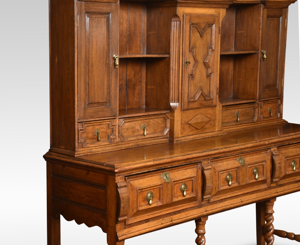 A Jacobean style oak dresser featuring geometric panel moulding, a central integrated clock, open upper shelves, and six barley twist legs. View XI