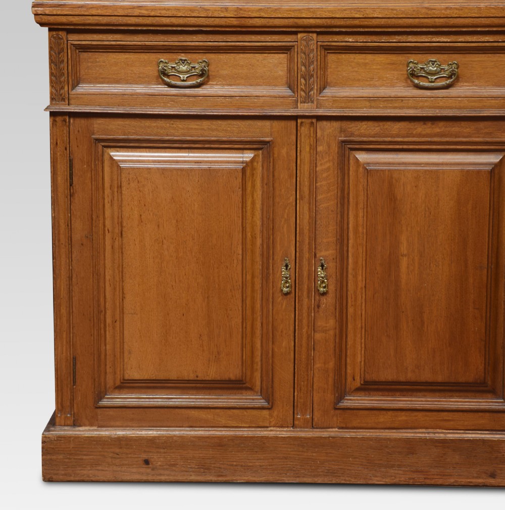 A large warm brown oak bookcase featuring three upper glazed doors with geometric astragal glazing, three drawers, and three panelled cupboard doors below. View II