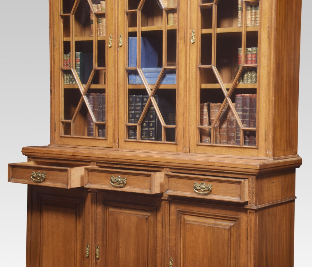A large warm brown oak bookcase featuring three upper glazed doors with geometric astragal glazing, three drawers, and three panelled cupboard doors below. View VII