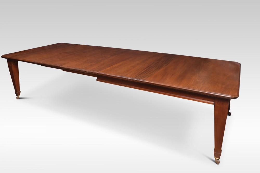 A large rectangular warm brown walnut extending dining table with tapered legs on brass castors.