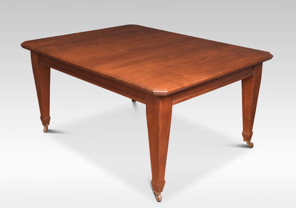A large rectangular warm brown walnut extending dining table with tapered legs on brass castors. View II