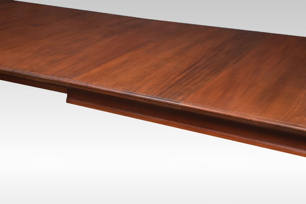 A large rectangular warm brown walnut extending dining table with tapered legs on brass castors. View III