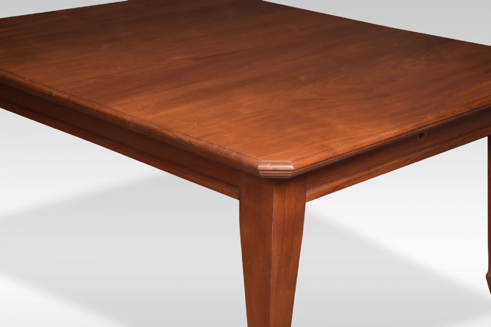 A large rectangular warm brown walnut extending dining table with tapered legs on brass castors. View V