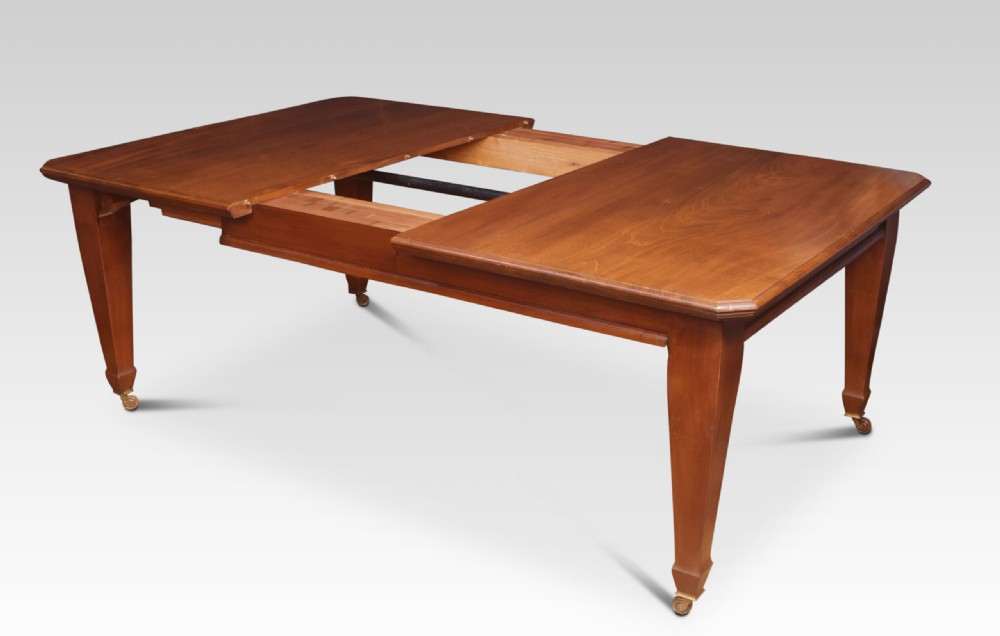 A large rectangular warm brown walnut extending dining table with tapered legs on brass castors. View VII
