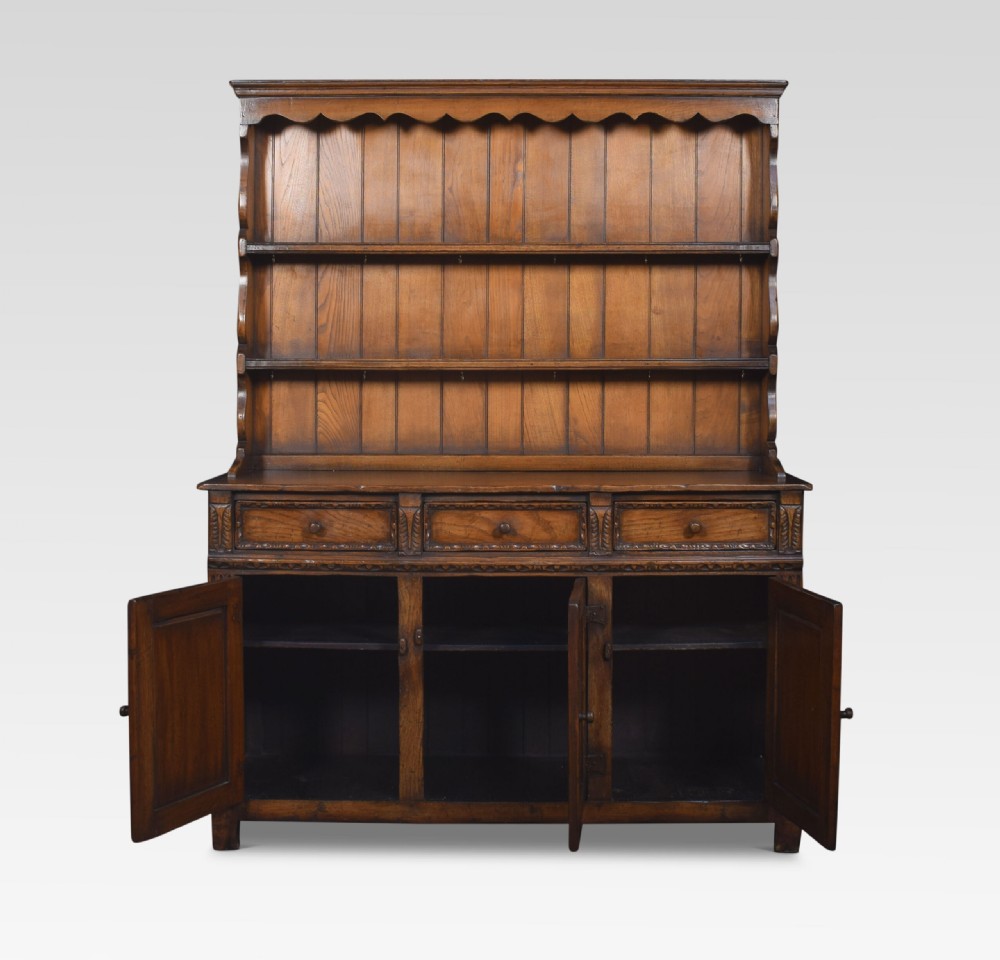 A Jacobean style dark oak dresser featuring a tiered open plate rack above three drawers and three carved panelled cupboard doors. View III