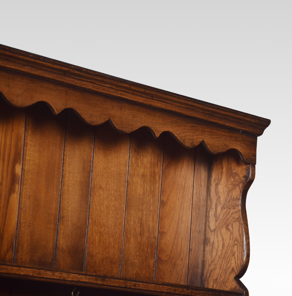 A Jacobean style dark oak dresser featuring a tiered open plate rack above three drawers and three carved panelled cupboard doors. View VIII