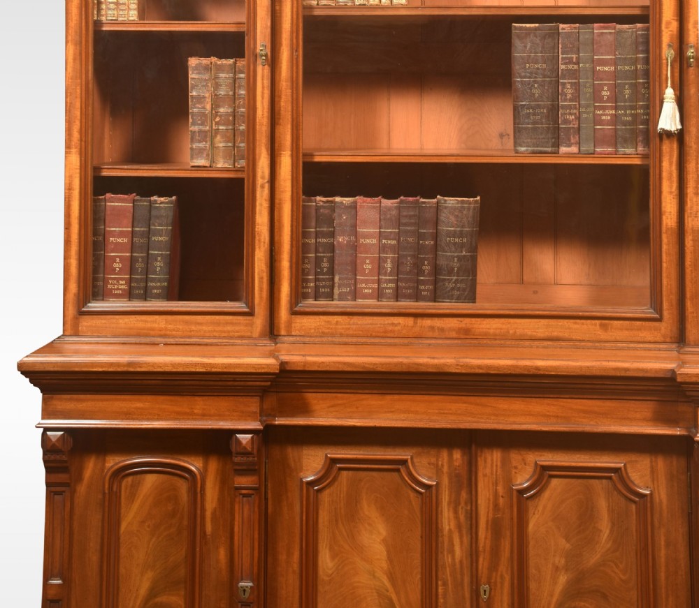 A large Victorian flame mahogany four-door breakfront library bookcase featuring arched glazed upper doors and panelled lower cupboard doors. View II