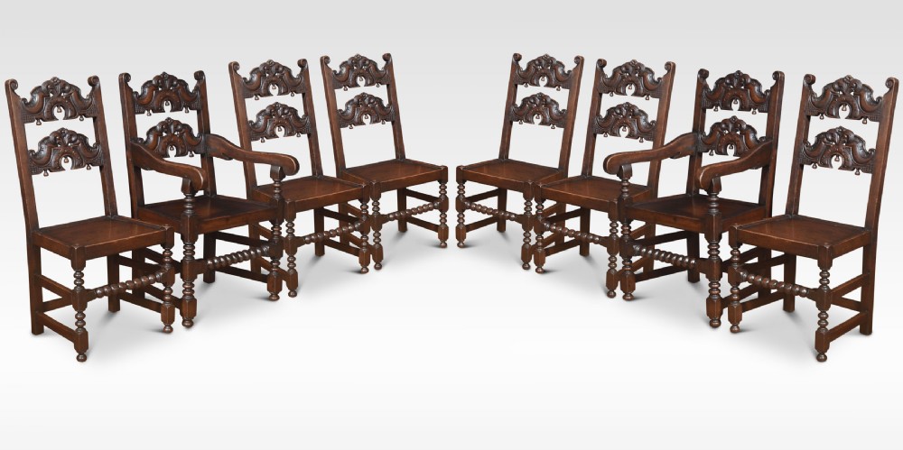 A set of eight dark oak dining chairs consisting of six side chairs and two carvers with carved back rails and turned front legs.
