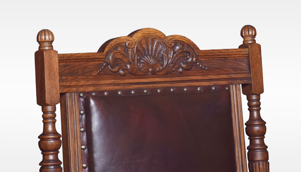 A pair of antique Victorian carved oak library armchairs upholstered in dark brown leather with brass studding and turned front legs on castors. View II