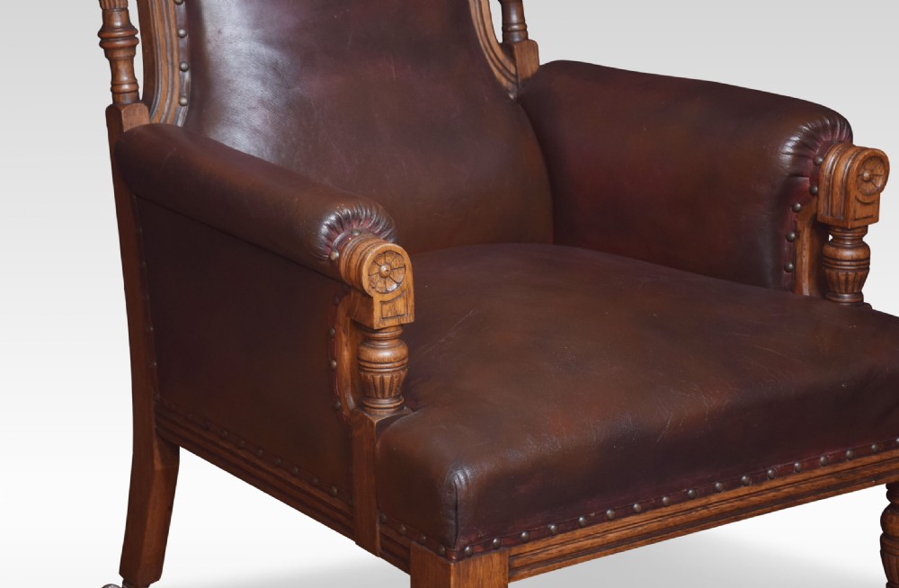 A pair of antique Victorian carved oak library armchairs upholstered in dark brown leather with brass studding and turned front legs on castors. View III