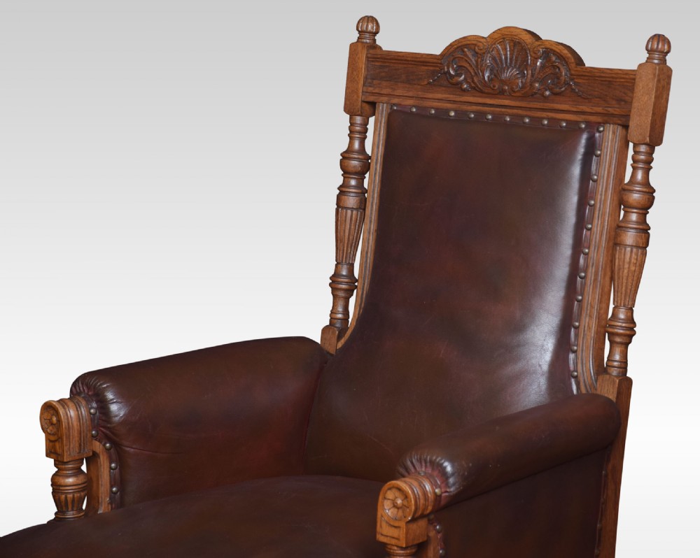 A pair of antique Victorian carved oak library armchairs upholstered in dark brown leather with brass studding and turned front legs on castors. View VI