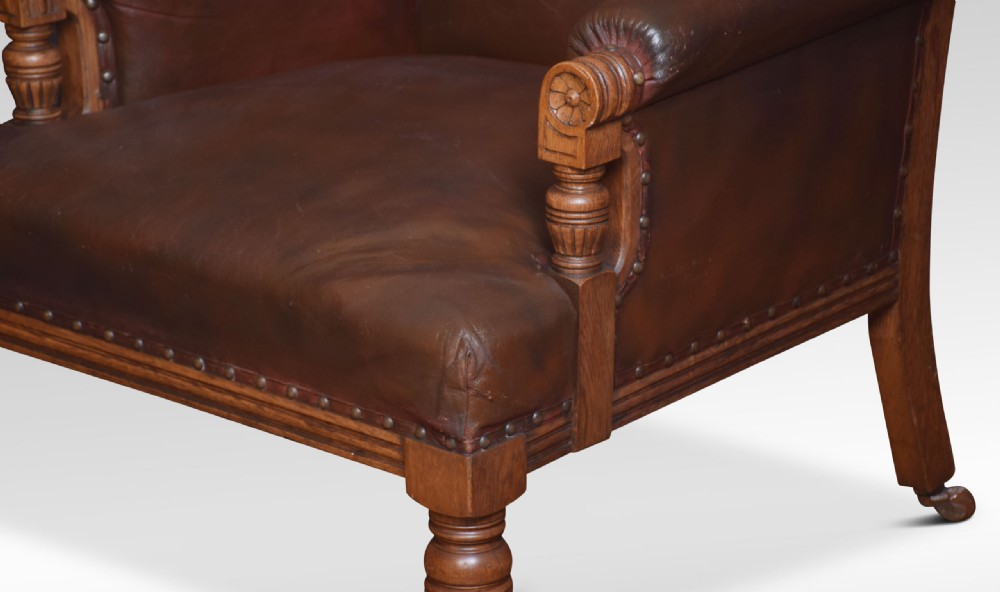 A pair of antique Victorian carved oak library armchairs upholstered in dark brown leather with brass studding and turned front legs on castors. View VII