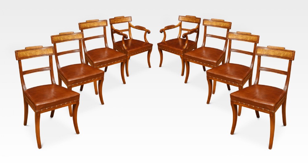 A set of eight Regency mahogany dining chairs featuring brown leather seats with brass stud detail, tablet top rails, and sabre legs.