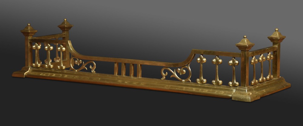 An antique solid brass Art Nouveau fireplace fender featuring stylized balusters, organic scrollwork motifs, and raised corner posts.