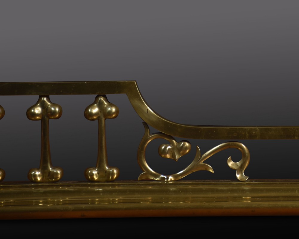 An antique solid brass Art Nouveau fireplace fender featuring stylized balusters, organic scrollwork motifs, and raised corner posts. View III
