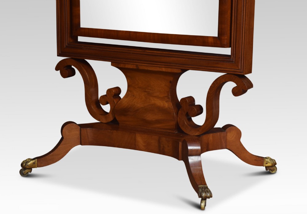 A Regency period mahogany cheval mirror featuring spiral-turned upright columns, finials, and a rectangular tilting frame resting on splayed legs with brass lion paw castors. View II
