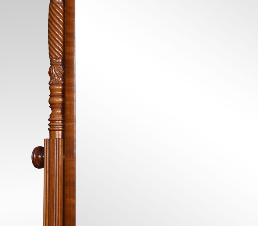 A Regency period mahogany cheval mirror featuring spiral-turned upright columns, finials, and a rectangular tilting frame resting on splayed legs with brass lion paw castors. View V