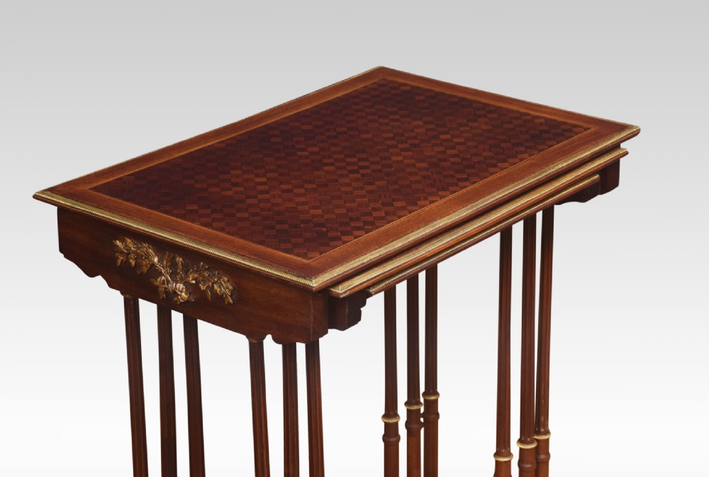 A set of three nesting walnut side tables featuring geometric parquetry tops, slender turned legs, and brass mounts. View V