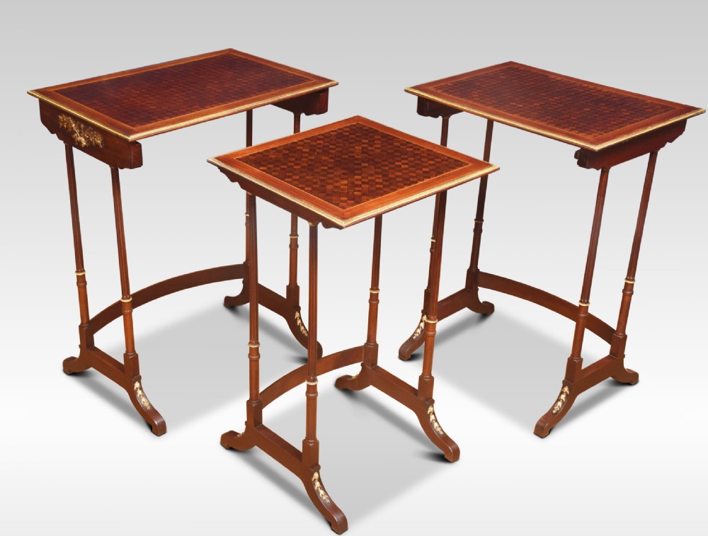 A set of three nesting walnut side tables featuring geometric parquetry tops, slender turned legs, and brass mounts. View VI