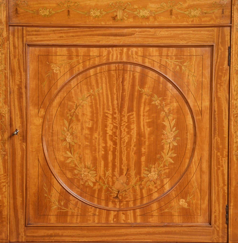 A late 19th-century satinwood side cabinet featuring intricate floral marquetry inlay, a central circular wreath medallion on a single panelled door, and square tapered legs. View II