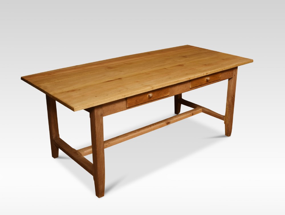 A large rectangular light brown wooden refectory dining table featuring two drawers along the front frieze and an H-stretcher base.
