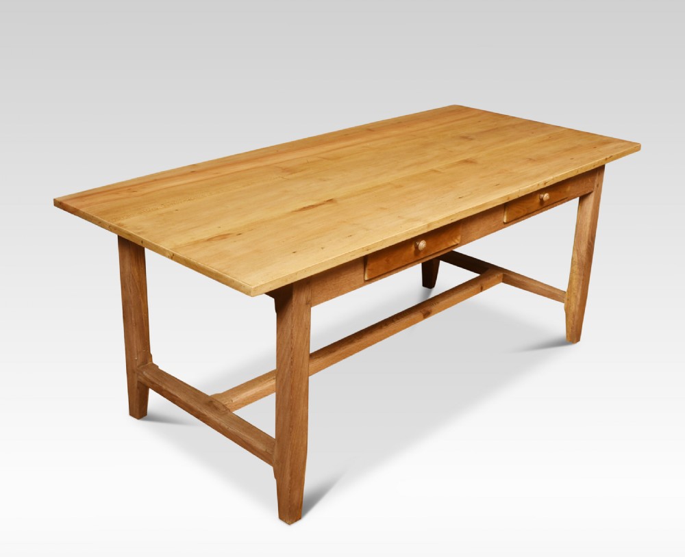 A large rectangular light brown wooden refectory dining table featuring two drawers along the front frieze and an H-stretcher base. View II