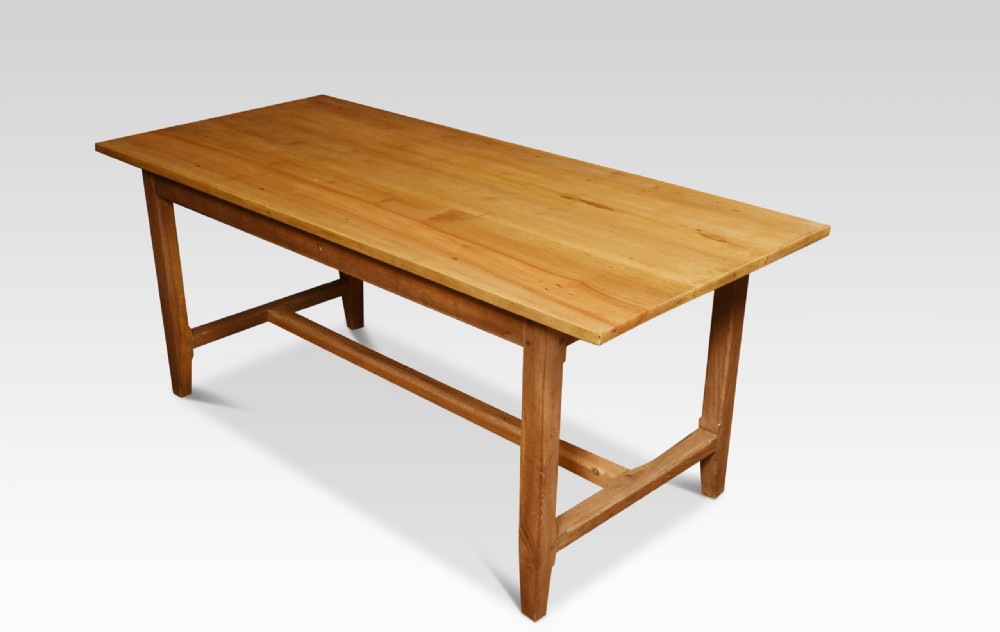 A large rectangular light brown wooden refectory dining table featuring two drawers along the front frieze and an H-stretcher base. View V