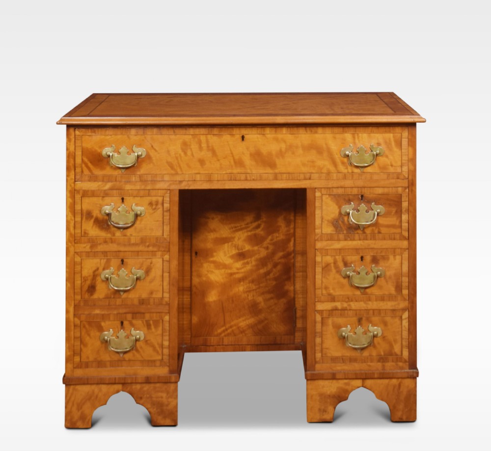 A George III style satinwood kneehole desk featuring crossbanded drawers, brass batwing handles, a central recessed cupboard, and bracket feet. View II