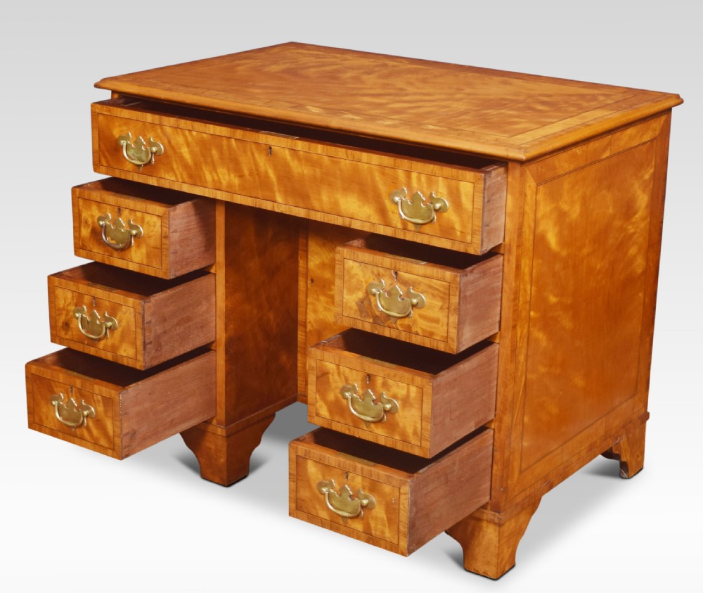 A George III style satinwood kneehole desk featuring crossbanded drawers, brass batwing handles, a central recessed cupboard, and bracket feet. View V