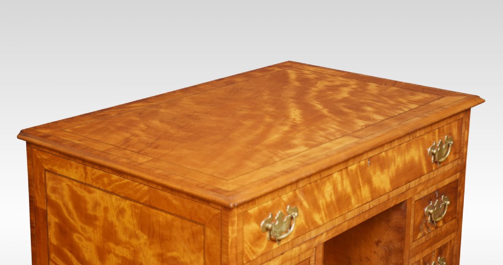 A George III style satinwood kneehole desk featuring crossbanded drawers, brass batwing handles, a central recessed cupboard, and bracket feet. View VII