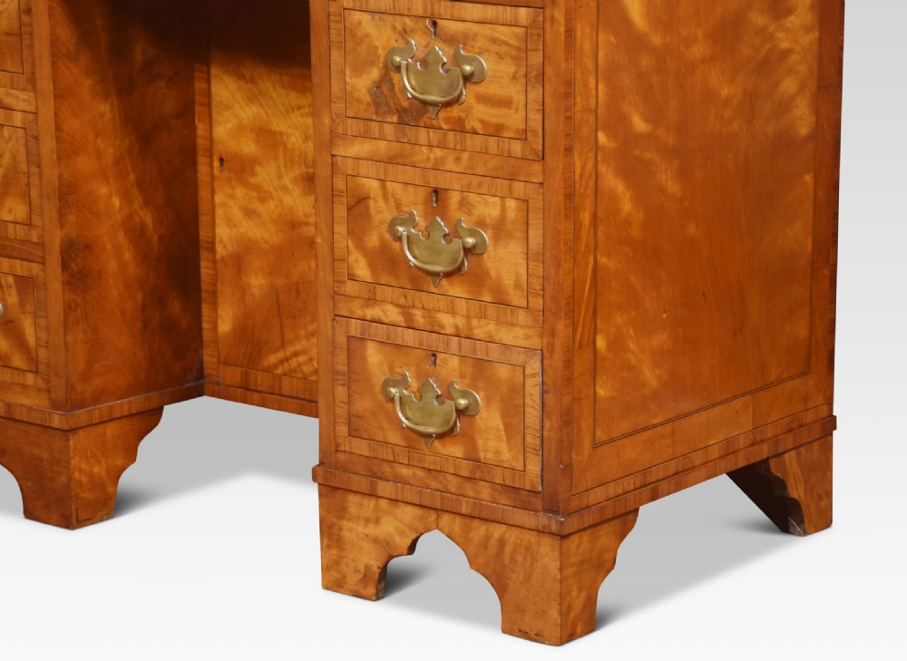 A George III style satinwood kneehole desk featuring crossbanded drawers, brass batwing handles, a central recessed cupboard, and bracket feet. View IX