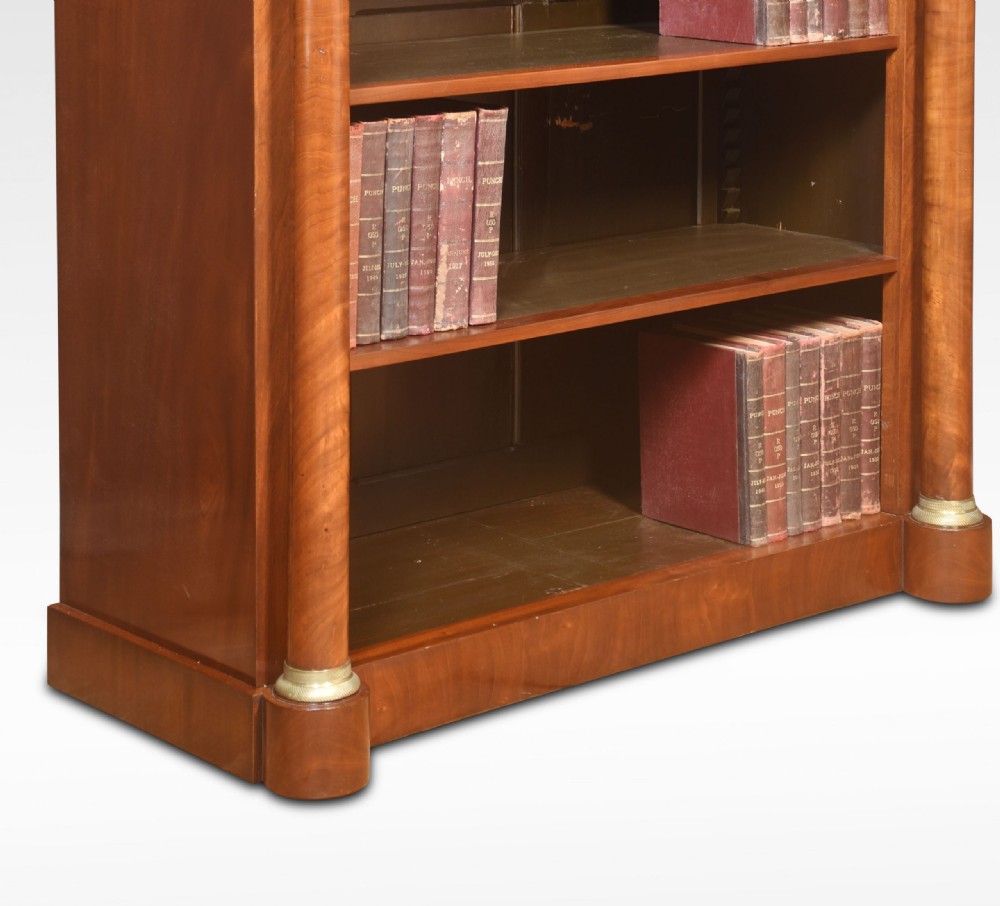 A tall open mahogany bookcase featuring classical flanking columns with brass capitals and adjustable interior shelving. View V